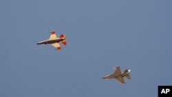 ເຮື​ບິນ​ລົບກອງ​ທັບ​ອາ​ກາດ F-16 ທີ່​ໃຊ້​ປັນ​ຍາ​ປະ​ດິດ​ບັນ​ຊາ, ຊ້າຍ, ບິນ​ຢູ່​ທາງ​ຂ້າງ​ເຮືອ​ບິນລົບ F-16 ທີ່​ສົມ​ມຸດ​ວ່າ​ເປັນ​ສັດ​ຕູ ພະ​ຍາ​ຍາມ​ທີ່​ຈະ​ບັງ​ຄັບ​ຄູ່​ຕໍ່​ສູ້​ຂອງ​ມັນ​ໄປ​ຈຸດ​ທີ່​ມີ​ຄວາມ​ສ່ຽງ, ຢູ່​ເທິງ​ຖານ​ທັບ​ອາ​ກາດ ເອັດ​ເຫວີດ​ສ໌, ລັດ​ຄາ​ລິ​ຟໍ​ເນຍ, 2 ພຶດ​ສະ​ພາ 2024.