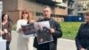 Lider Ekološkog ustanka Aleksandar Jovanović Ćuta pokazuje plakat peticije za podizanje spomen obeležja na mestu uništene zgrade Generalštaba VS i portret funkcionera vladajuće SNS Gorana Vesića, ispred zgrade Generalštaba u Beogradu, 15. marta 2024. (Foto: VoA/Rade Ranković)