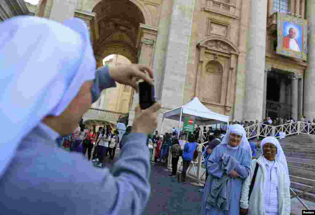 Nuns pose in front of a tapestry featuring Pope John Paul II in St. Peter's Square at the Vatican.