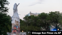 Police walk around at the site of the covered Christopher Columbus statue after protesters attempted to topple the statue located in Roosevelt and Columbus Dr. in Chicago, July 17, 2020. (Credit: Tyler LaRiviere/Chicago Sun-Times)
