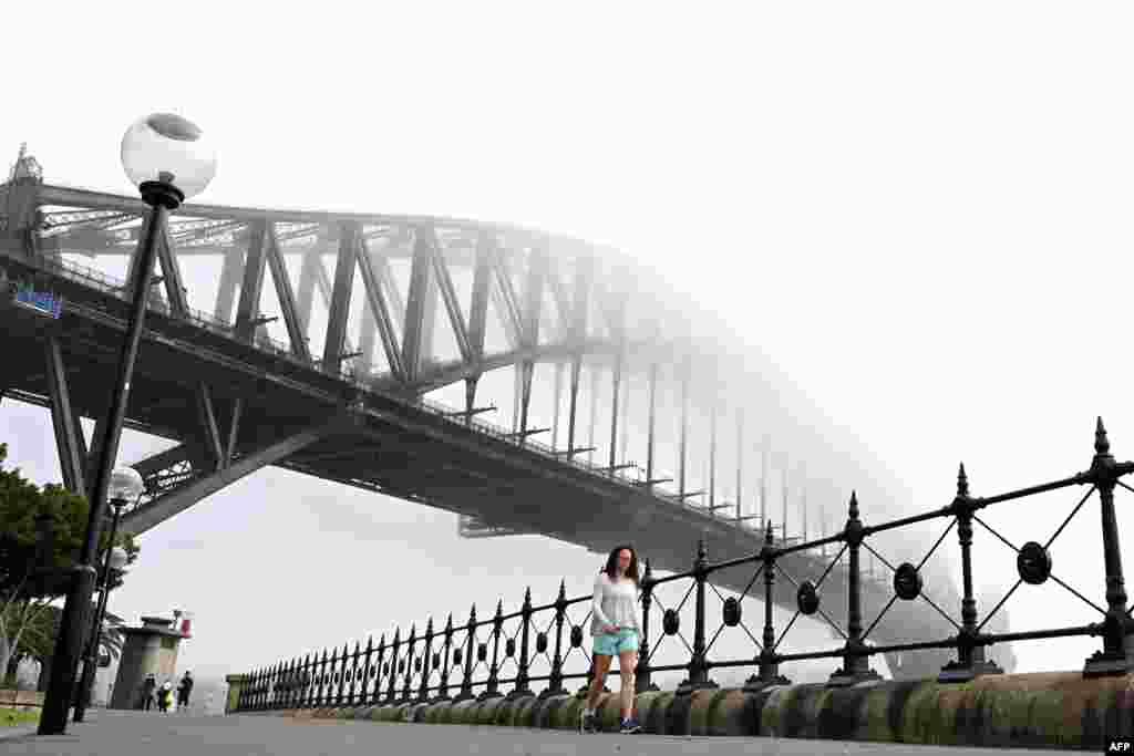 People walk under Australia&#39;s iconic landmark Harbour Bridge in Sydney, Australia, as heavy fog blankets the city.