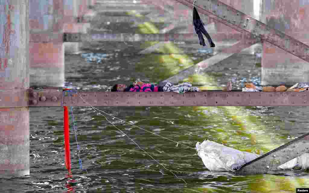 A man sleeps on a girder between the two pillars of a bridge on the Sabarmati river during a hot day in Ahmedabad, India.