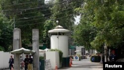 FILE - A policeman and private security personnel stand guard at the entrance of a road leading towards the U.S. consulate in Lahore, Aug. 9, 2013.