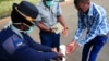 Un officier de police montre à un visiteur comment désinfecter ses mains contre la propagation du coronavirus à Harare au Zimbabwe, le 19 mars 2020.