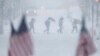 People walk across a snow-covered intersection behind American flags in Hoboken, New Jersey, Feb. 9, 2017.
