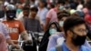 FILE - A woman wearing a face mask rides as a passenger on a motorbike amid a rush of people outside a market, amid the coronavirus pandemic, in Karachi, Pakistan, June 8, 2020.