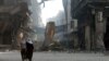 Syrians walk past anti-sniper curtains remaining in a street on May 12, 2014 in a destroyed neighbourhood of the Old City of Homs.