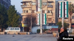 Seorang pria tampak merokok saat ia duduk di pinggir jalan dekat bendera Suriah di Aleppo, satu bulan sejak pemerintahan Presiden Bashar al-Assad terguling, pada 8 Januari 2025. (Foto: Reuters/Karam al-Masri)