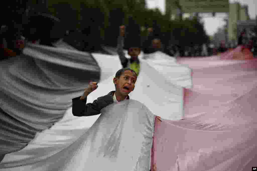 A boy chants slogans through a gap in a national flag raised by Shiite rebels, known as Houthis, during a protest against Saudi-led airstrikes in Sanaa, Yemen.