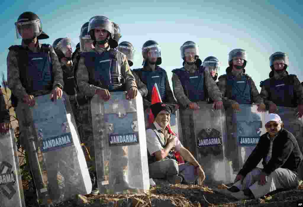 A man sits with a national flag as paramilitary police officers block thousands of people outside the Silivri jail complex in Silivri, Turkey.
