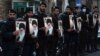Sejumlah petugas kepolisian Iran menunjukkan poster Pemimpin Tertinggi Iran Ayatollah Ali Khamenei saat melindung Kedutaan Besar Prancis saat demo memprotes karikatur Ali Khamenei oleh majalah Prancis Charlie Hebdo, di Teheran, Iran, 8 Januari 2023. (Foto: Vahid Salem/AP Photo)