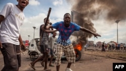 Para demonstran di depan mobil yang dibakar selama demonstrasi oposisi di Kinshasa, Republik Demokratik Kongo (19/9). (AFP/Eduardo Soteras)