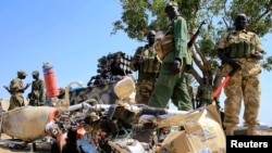 FILE - South Sudan army soldiers stand next to a destroyed motorcycle near Bor Airport, northwest of capital Juba, Dec. 25, 2013. 