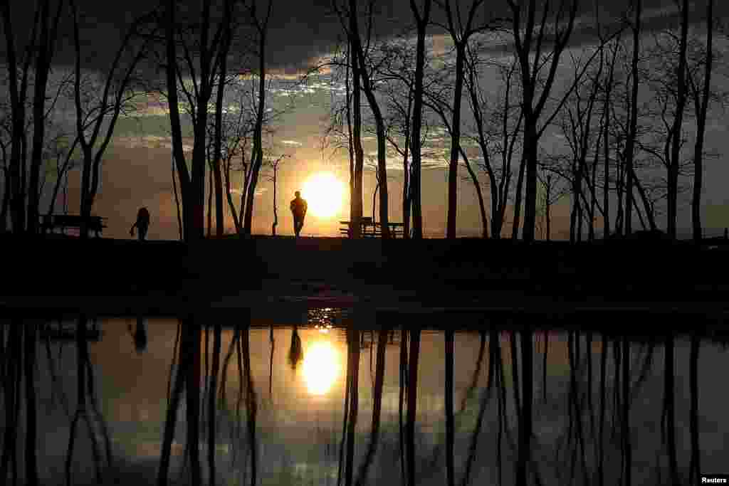 People stand and watch the sunset at Presque Isle State Park in Erie, Pennsylvania, USA, April 13, 2016.