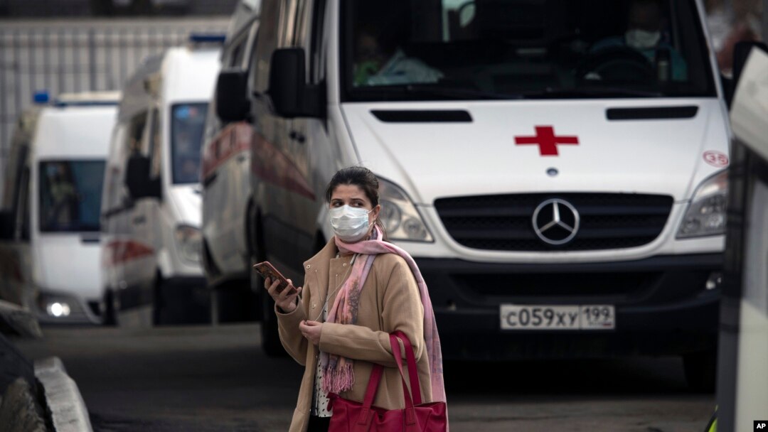 A woman wearing a face mask stands next to ambulances as they queue to transfer patients suspected of having the coronavirus infection to a hospital in Moscow, Russia, Thursday, April 9, 2020.