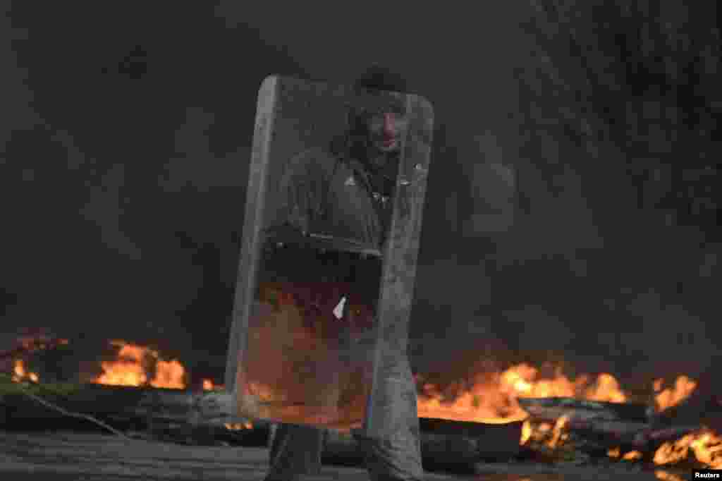 Seorang demonstran pro-Rusia memegang perisai di pos pemeriksaan, sementara asap hitam membubung dari ban-ban yang dibakar menyelimuti daerah di Slovyansk (13/4). (Reuters/Maks Levin)