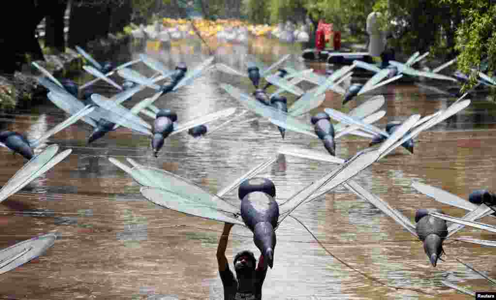 Seorang pria memperbaiki instalasi patung-patung capung di atas kanal kota Lahore, Pakistan.