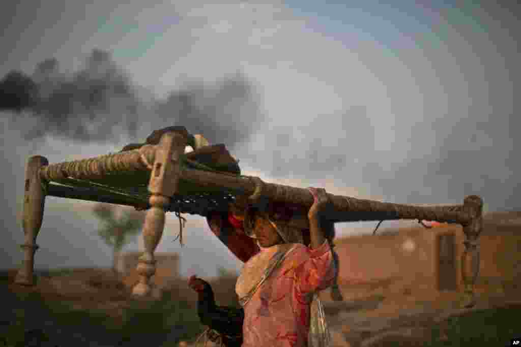 A Pakistani woman carrying a bed on her head and holding a rooster, walks back to her home through a brick factory on the outskirts of Islamabad, Pakistan.