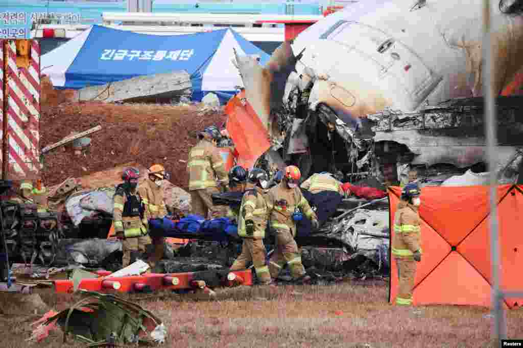 Firefighters carry the body of a passenger from the wreckage of an aircraft of Jeju Air that crashed after it went off the runway at Muan International Airport, in Muan, South Korea. At least 179 people died in the plane crash.