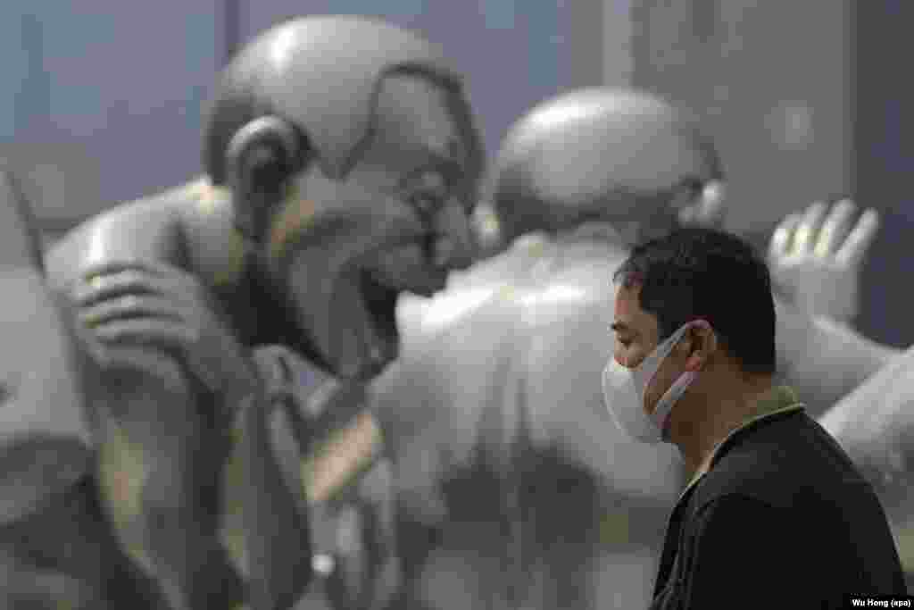 A Chinese man wearing a mask passes by a sculpture during a smoggy day in Beijing.