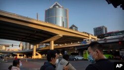 People wear face masks to protect against the spread of the new coronavirus as they wait to cross an intersection in Beijing, April 23, 2020.